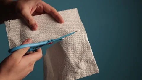 Hands cutting a paper towel with blue scissors on a teal background Stock Footage 340265908