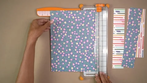 Hands Cutting Patterned Scrapbook Paper With Paper Trimmer On Craft Table Stock Footage 345617040