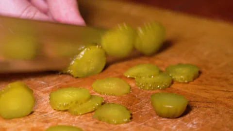 Hands is cutting a pickled cucumber with a knife on wooden board, close-up. Stock Footage 248088035