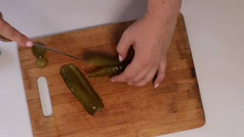 Hands cutting pickled cucumbers lengthwise on a wooden board with a sharp k.. Stock Footage 320954533