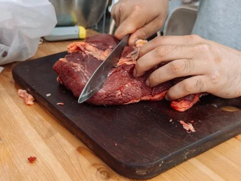 Hands cutting raw beef into smaller pieces on a cutting board before grinding Stock Photos