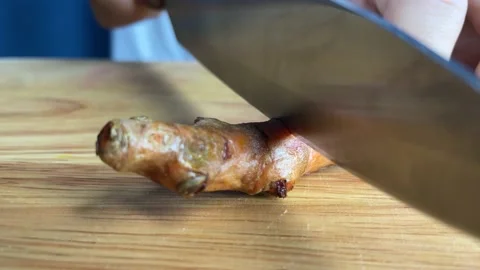Hands cutting raw turmeric root slice on a wooden chopping board at kitchen Stock Footage 233284573