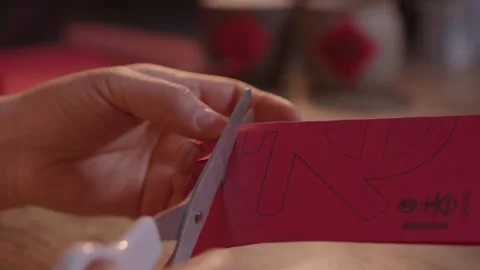 Hands Cutting Red Paper with Scissors on Wooden Table Stock Footage 336546821