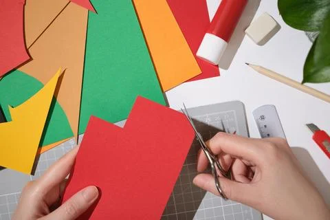 Hands cutting red paper with scissors on a creative workspace, colorful she.. Stock Photos