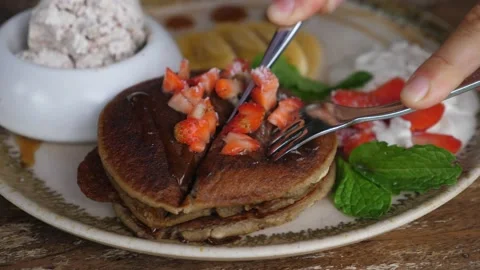 Hands cutting stack of pancakes with fork and knife. Healthy plant based Stock Footage 149877239