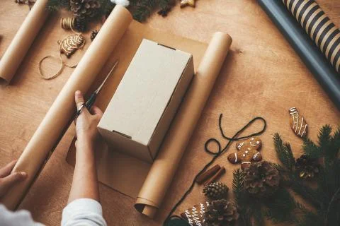 Hands cutting wrapping paper with scissors and gift box, pine branches, cones Stock Photos