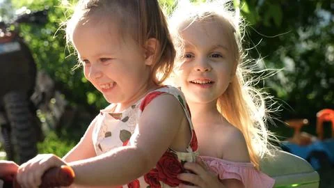 Hands of daddy pushes two little daughters on big toy motorcycle in summer .. Stock Photos