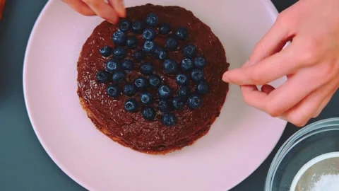 Hands Decorating Dark Brown Pancake with Blueberries on Pink Plate Indoors Vidéo 342862996