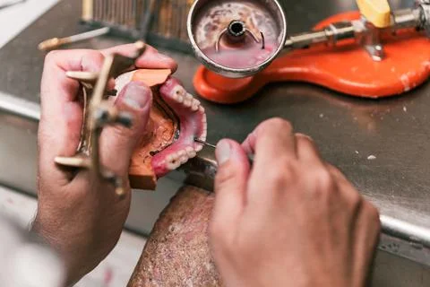 Hands of a dental technician fixing the paste on a dental prosthesis Stock Photos