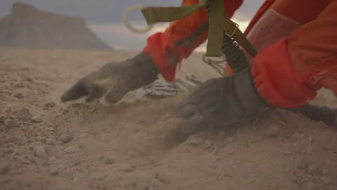 Hands digging in the desert while wearing orange overalls during sunset Stock Footage 288820202