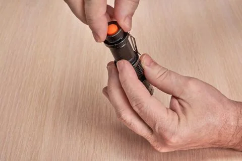 Hands disassemble a small black flashlight to replace a used battery Stock Photos