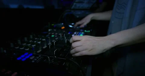 Hands of a DJ adjusting knobs and faders on a mixing console in a dark club Vídeo Stock 340004872