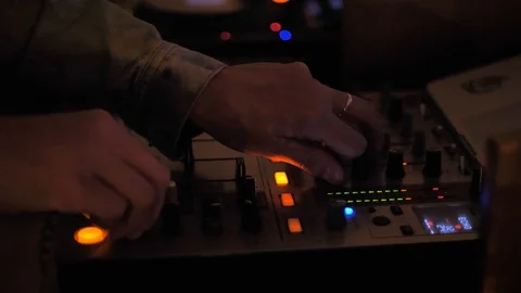 Hands of DJ close-up in a denim jacket. Blurry colored lights blink around. Stock Footage 120337801