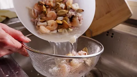 Hands Drain Shrimp Squid and Mussels in a Metal Colander Over a Kitchen Sink, Sh Stock Footage 341974028