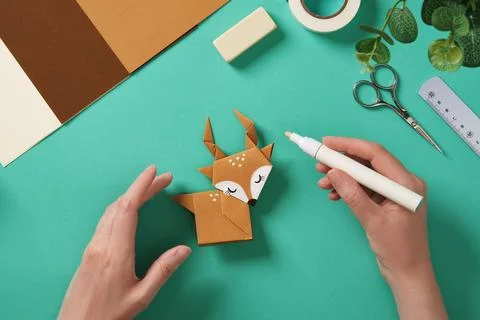Hands draw white dots with a marker on a paper reindeer craft. Around them .. Stock Photos