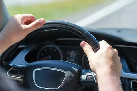 Hands of a driver gripping a steering wheel while driving on a sunny day Stock Photos