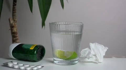 Hands drop a lime slice into a glass of water beside medicine and a tissue Stock-Footage 316038684