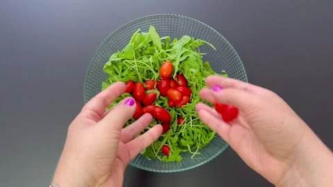 Hands dropping fresh red cherry tomatoes into glass bowl filled  Stock Footage 345590789