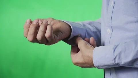 Hands of an elderly man buttoning the button on his shirt sleeve, on a green Stock Footage 163441944