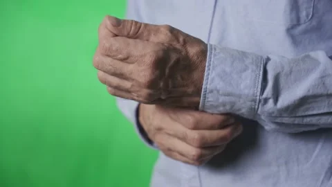 Hands of an elderly man buttoning the button on his shirt sleeve, on a green Stock Footage 166689503