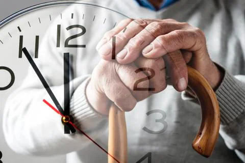 Hands of an elderly man on a cane over a clock Foto stock