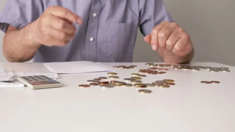 Hands of an elderly man counted his money. On the table are coins, bills and an Stock Footage 129819217