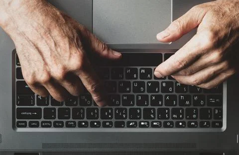 Hands of an elderly man learning to use computer, typing on a laptop, view fr Stock Photos