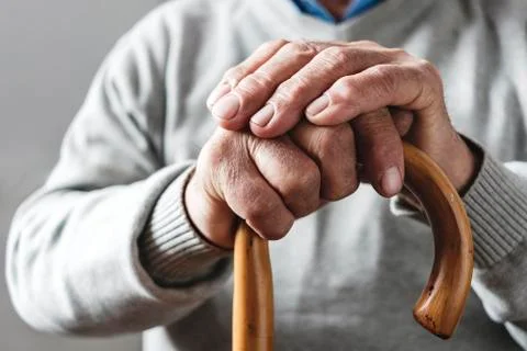 Hands of an elderly man resting on a walking cane Stock Photos