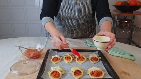 Hands of elderly woman smears delicious apple cakes lying on baking sheet Stock Footage