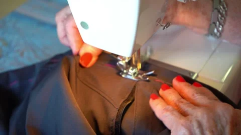 Hands of a eldlerly seamstress sewing a pair of pants on a sewing machine. Stock Footage 294722422