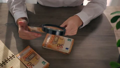 Hands examining euro banknotes with magnifying glass at desk, check authent.. Stock Footage 337179068