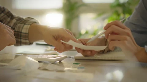 Hands exchanging documents during a collaborative planning session at a desk Stock Footage 323806832
