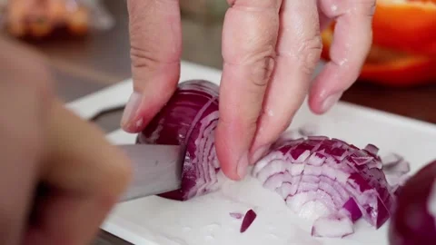 Hands expertly cutting a vibrant red onion on a white plate, surrounded by an Stock Footage 315313596