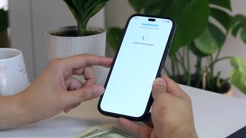 Hands explore online listings for mid-priced cars on a phone, with cash nearby Stock Footage 316038815