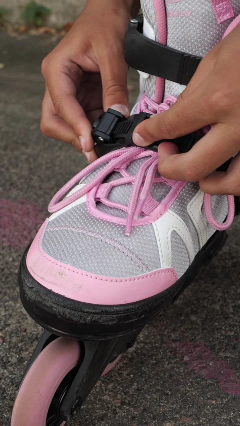 Hands fastening the buckle on a pink inline skate on pavement Stock Footage 342521150