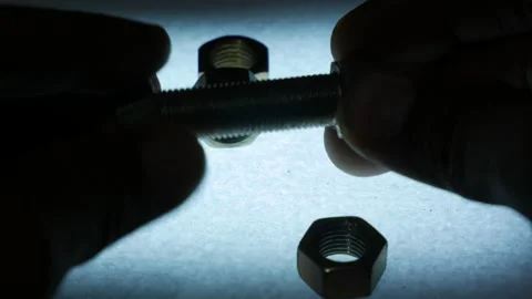 Hands Fastening Metal Hex Nut onto Bolt Surrounded by Nuts Stock Footage 340069998