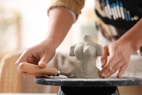 Hands of female sculptor with loop tool shaping clay figurine on pottery whee Stock Photos
