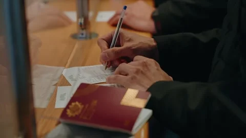 Hands filling out form at counter with red passport and boarding pass on desk Stock Footage 337914038
