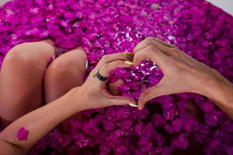 Hands fingers in the shape of a heart in bath with petals in tropics Stock Photos