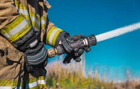 Hands of firefighter, no face, holding a hose by throwing water at high press Stock Photos