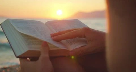 Hands flipping pages of a book while reading by the seaside at sunset in summer Video stock 317244873