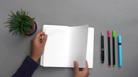 Hands flipping the pages of an empty notebook on a grey desk. 動画素材 147405515