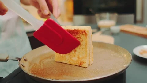 Hands flipping toast soaked in egg batter on stovetop in kitchen Stock Footage 342888869