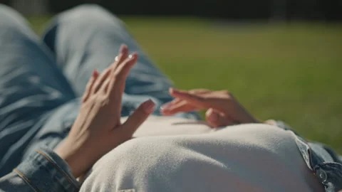 Hands floating above belly in grass, slow finger choreography, denim sleeve and Stock Footage 347336682