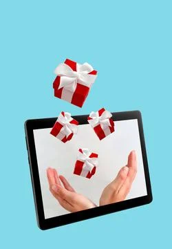 Hands with flying gift boxes on digital tablet screen on blue background. Stock Photos