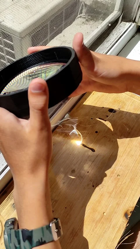 Hands focusing sunlight through a magnifying glass to ignite a small object on a Stock-Footage 298024337