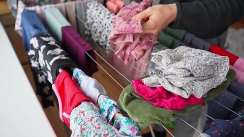 Hands fold and stack colorful children’s clothes taken from an indoor drying 動画素材 327896869
