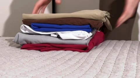 Hands fold clothes on a bed. Neat laundry stacking creates organized home s.. Stock Footage 335465907