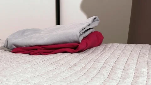 Hands fold clothes on a bed. Neat laundry piles are arranged in a home bedr.. Stock Footage 335830151