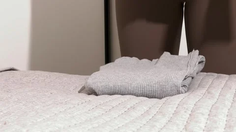 Hands fold knit clothes on a bed. A person stacks a sweater in a tidy home .. Stock Footage 335830159